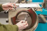 Engineering trainee adjusting metal component in manual lathe chuck