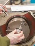 Engineering trainee adjusting metal component in manual lathe chuck